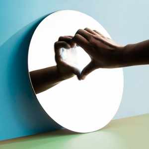 Hand forming a heart in a round mirror against a blue wall, symbolizing relationship anxiety