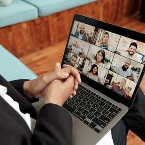 Hands clasped on a laptop with a video call showing a small group therapy session