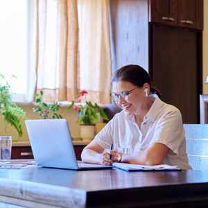 Woman at dining table smiling at open laptop during online individual therapy