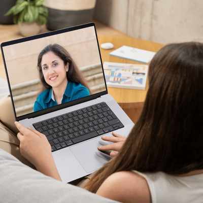 Woman on couch in video session with therapist Marisa Knight on laptop screen