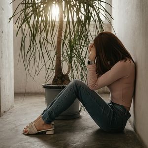 A woman sits on the floor with hear head in her hands as she struggles with anxious attachment style before online therapy