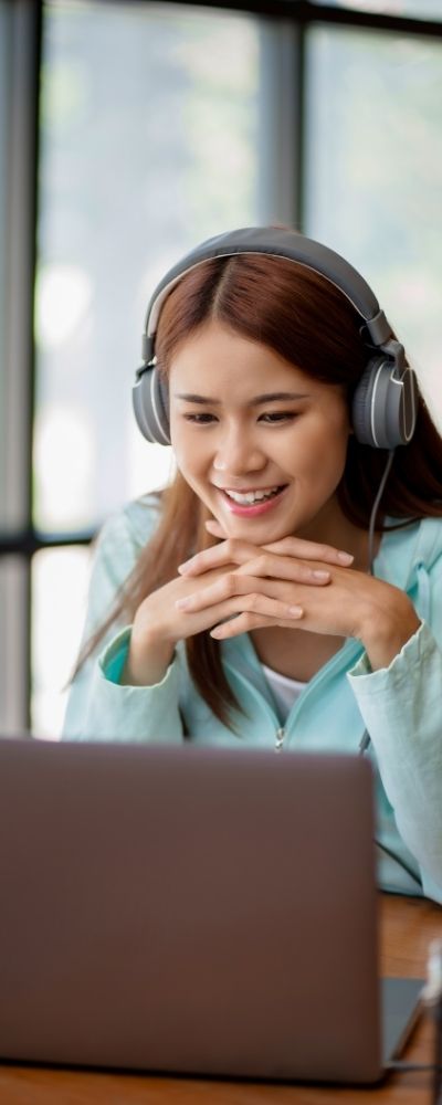 A woman smiling at her laptop with headphones on during an adjunct EMDR session
