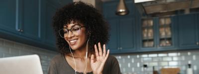 A woman waves at her laptop camera at the start of her therapy telehealth appointment